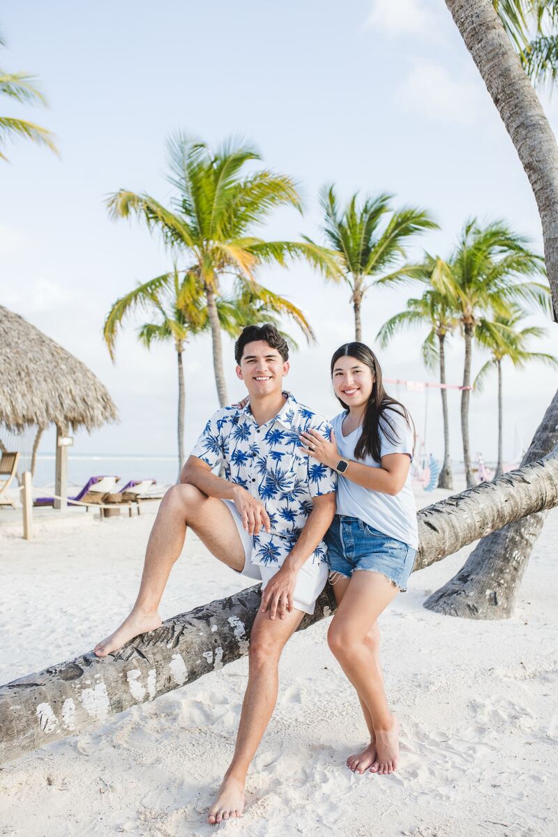 Me and my fiancée Karina sitting on a leaning palm tree on a white-sand beach